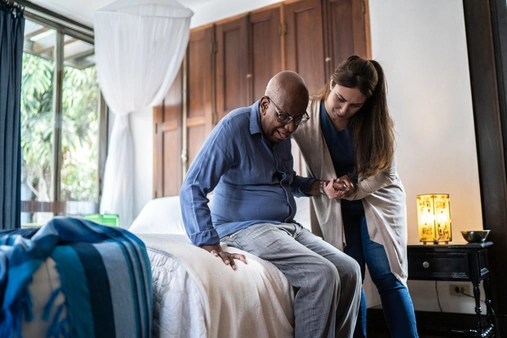 sitter helping elderly man get up from bed